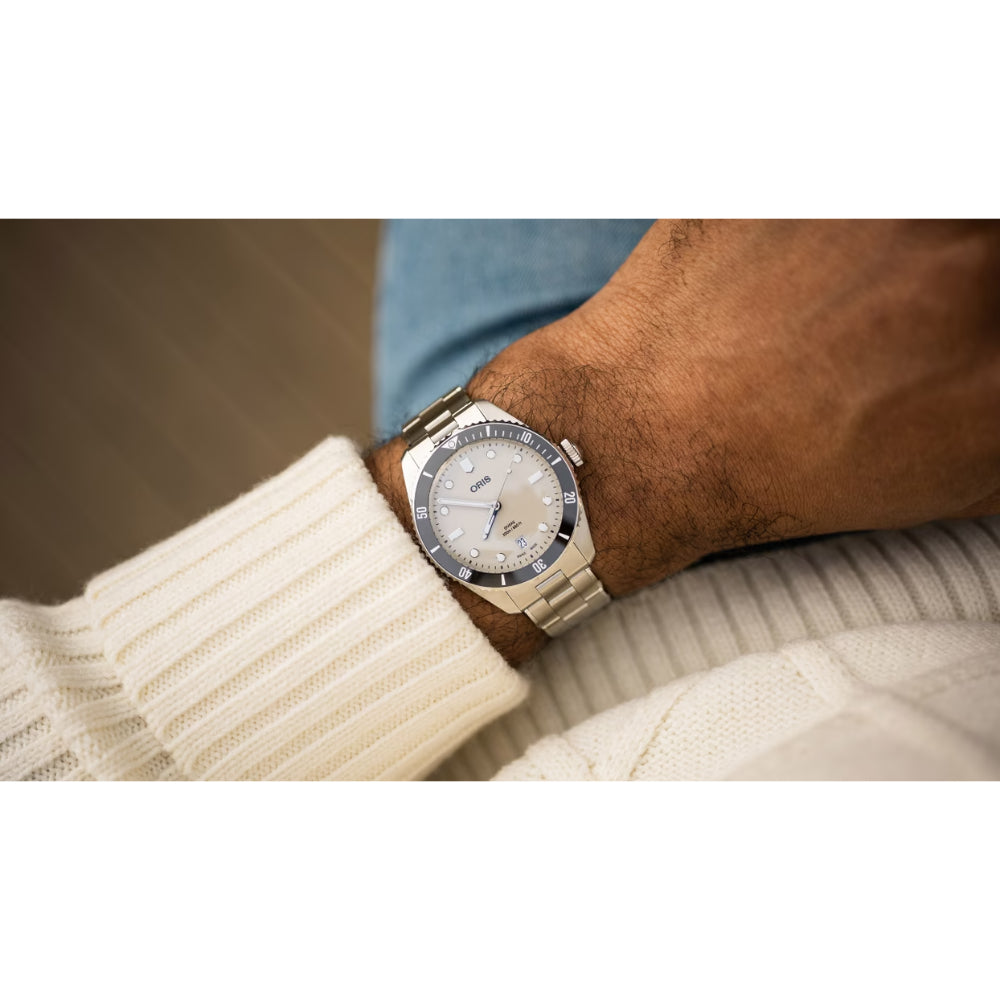 A silver stainless steel wristwatch with a white dial and blue bezel, worn on a person's wrist over a cream ribbed knit sweater.