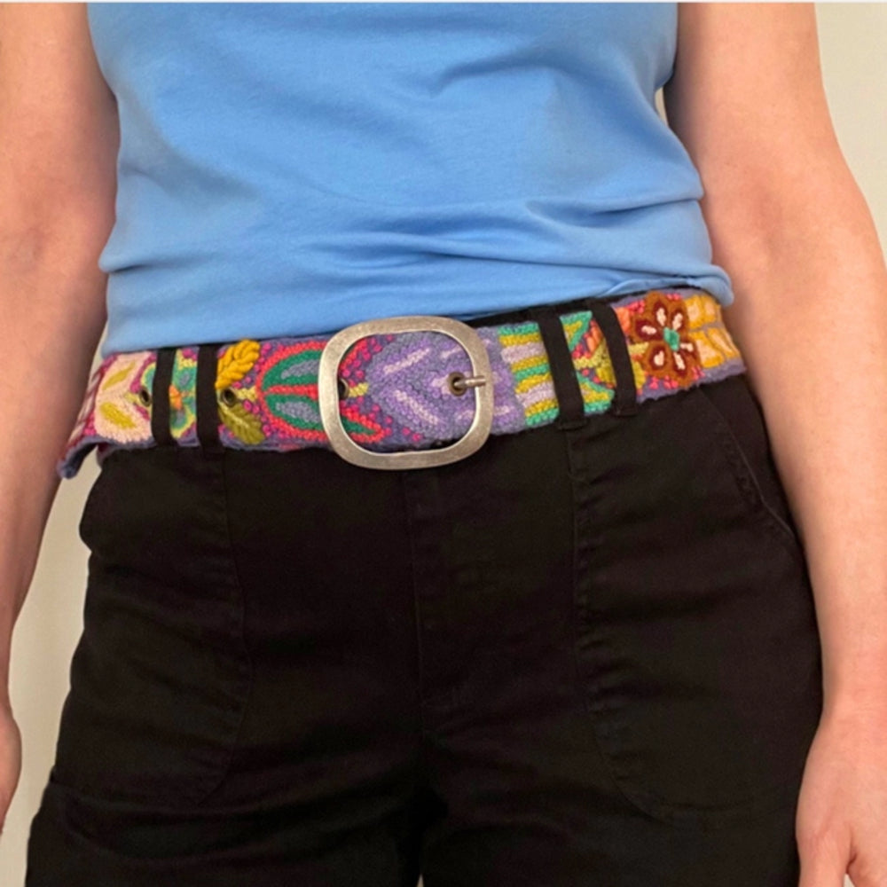 Person wearing a colorful belt with a large buckle on a plain background