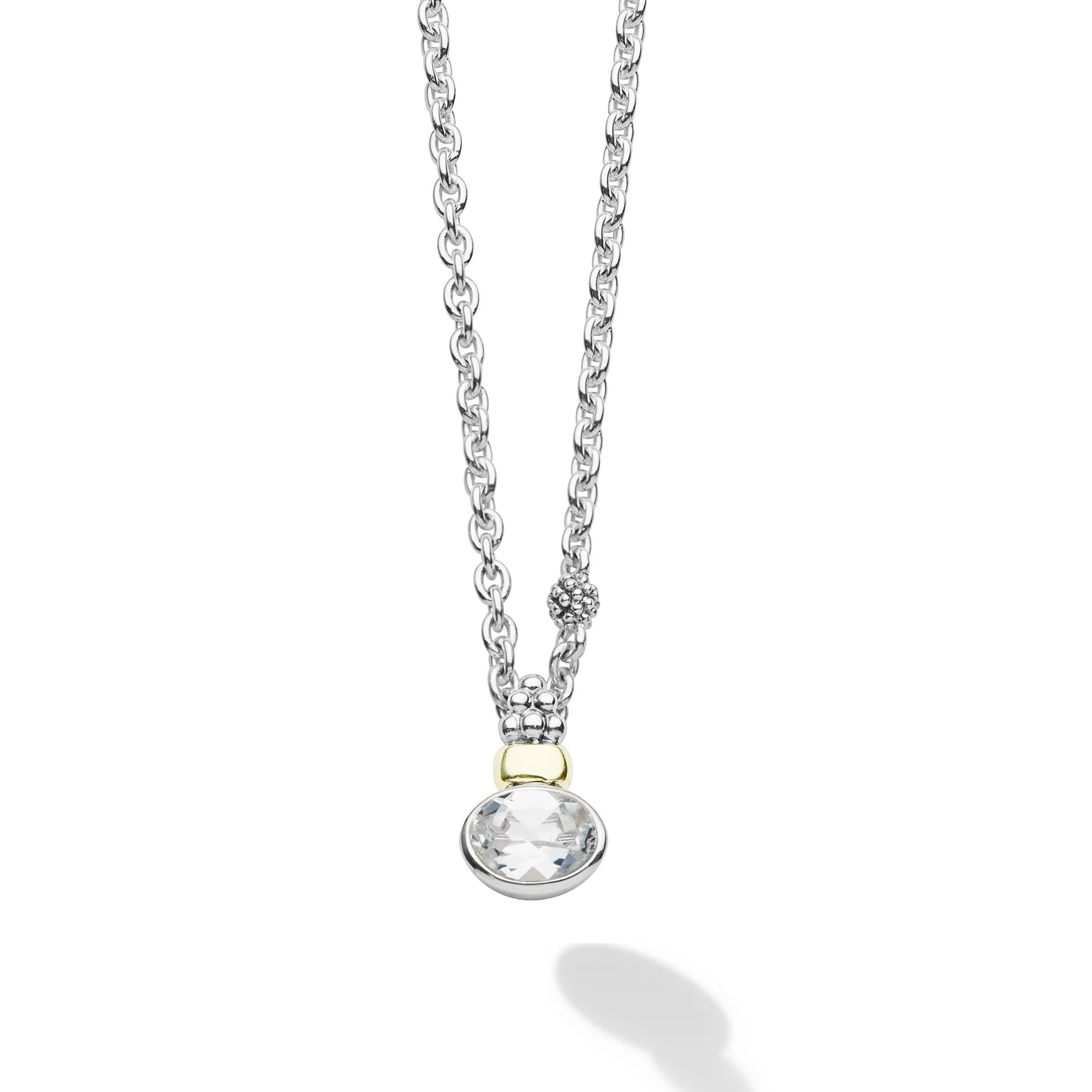 A silver chain necklace with a round bezel-set clear gemstone pendant, accented by a small gold detail at the top, shown on a white background with a soft shadow.