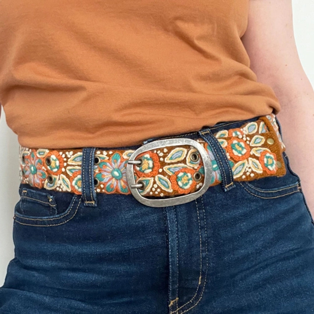 Person wearing a colorful belt with floral pattern and large buckle.