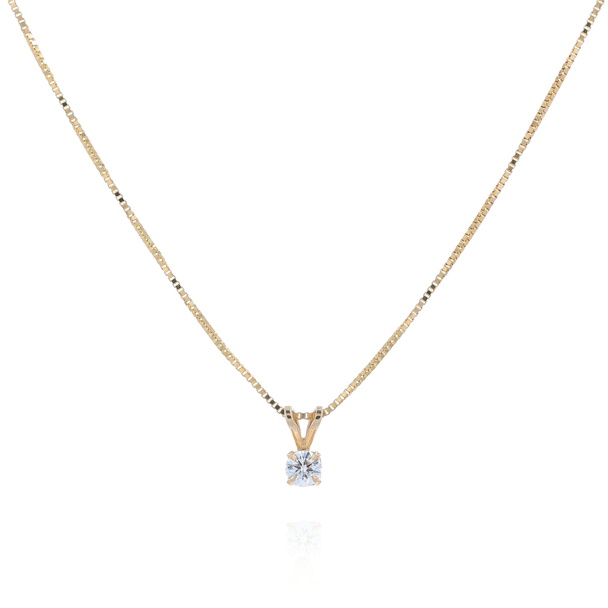 A delicate gold chain necklace with a small pendant holding a clear round-cut diamond, displayed against a solid white background.