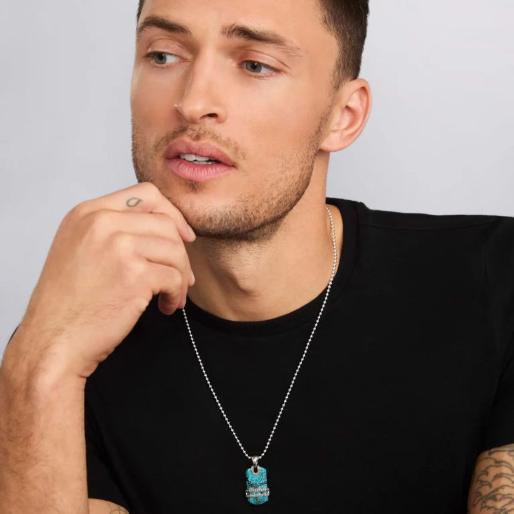 A close-up of a man wearing a silver ball-chain necklace with a rectangular turquoise pendant