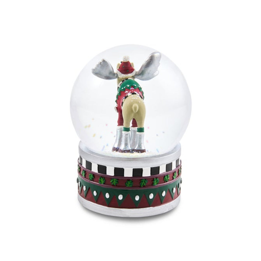 A novelty Christmas snow globe featuring a small figurine of a moose from behind wearing a green and red Santa hat and scarf, and boots, inside a clear glass sphere on a patterned red, green, and silver base.