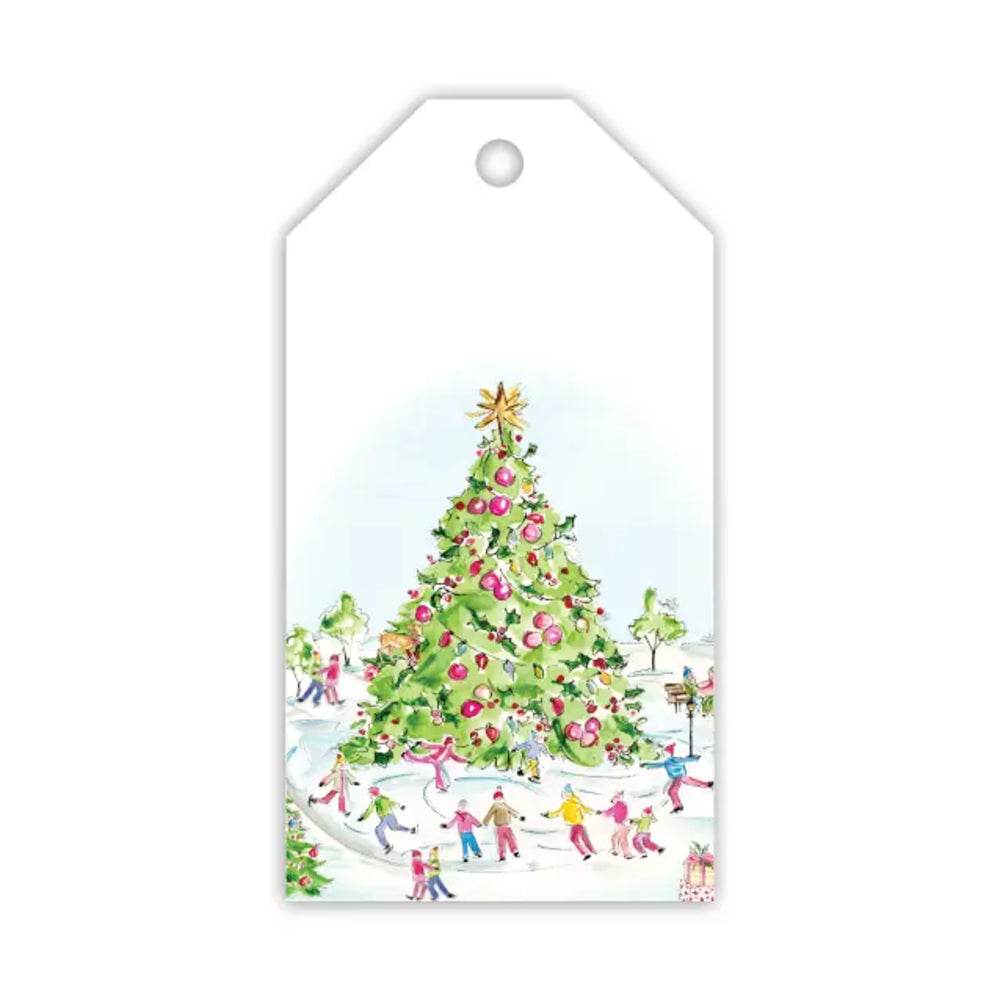 A white gift tag with a hanging hole at the top, featuring a watercolor-style illustration of a decorated Christmas tree and small children playing in the snow around it.