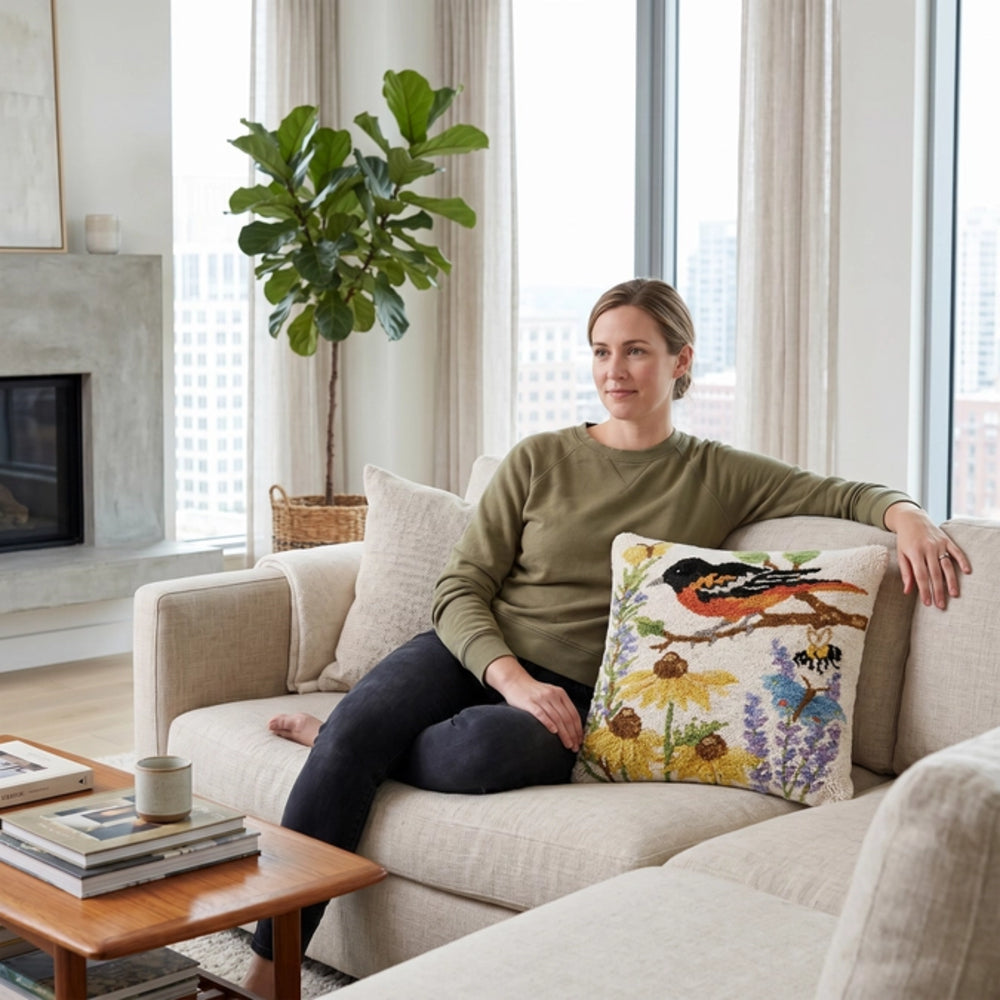 Woman sitting on a couch with a decorative pillow featuring birds and flowers in a living room.