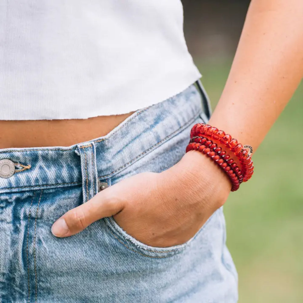 Person wearing blue jeans and a white top with a red hair tie on a blurred natural background