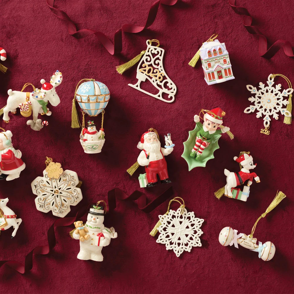 A collection of Christmas ornaments arranged on a dark burgundy fabric background with red ribbon garlands. The ornaments include Santa Claus, a snowman, a hot air balloon, a boot-shaped ornament, a house ornament, snowflakes, a reindeer, and other festive figures.