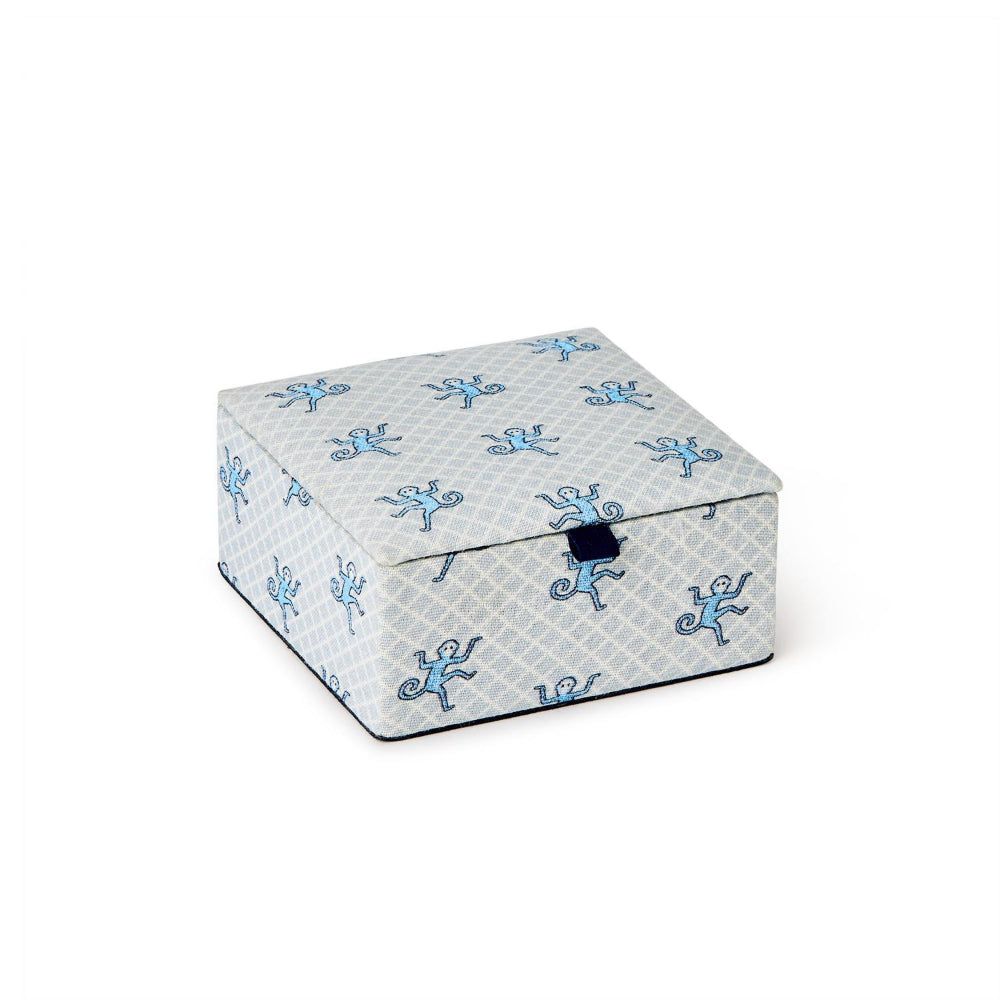 A square fabric storage box with a light gray and white geometric pattern, decorated with blue cartoon monkey motifs, featuring a dark blue snap button closure on the front.