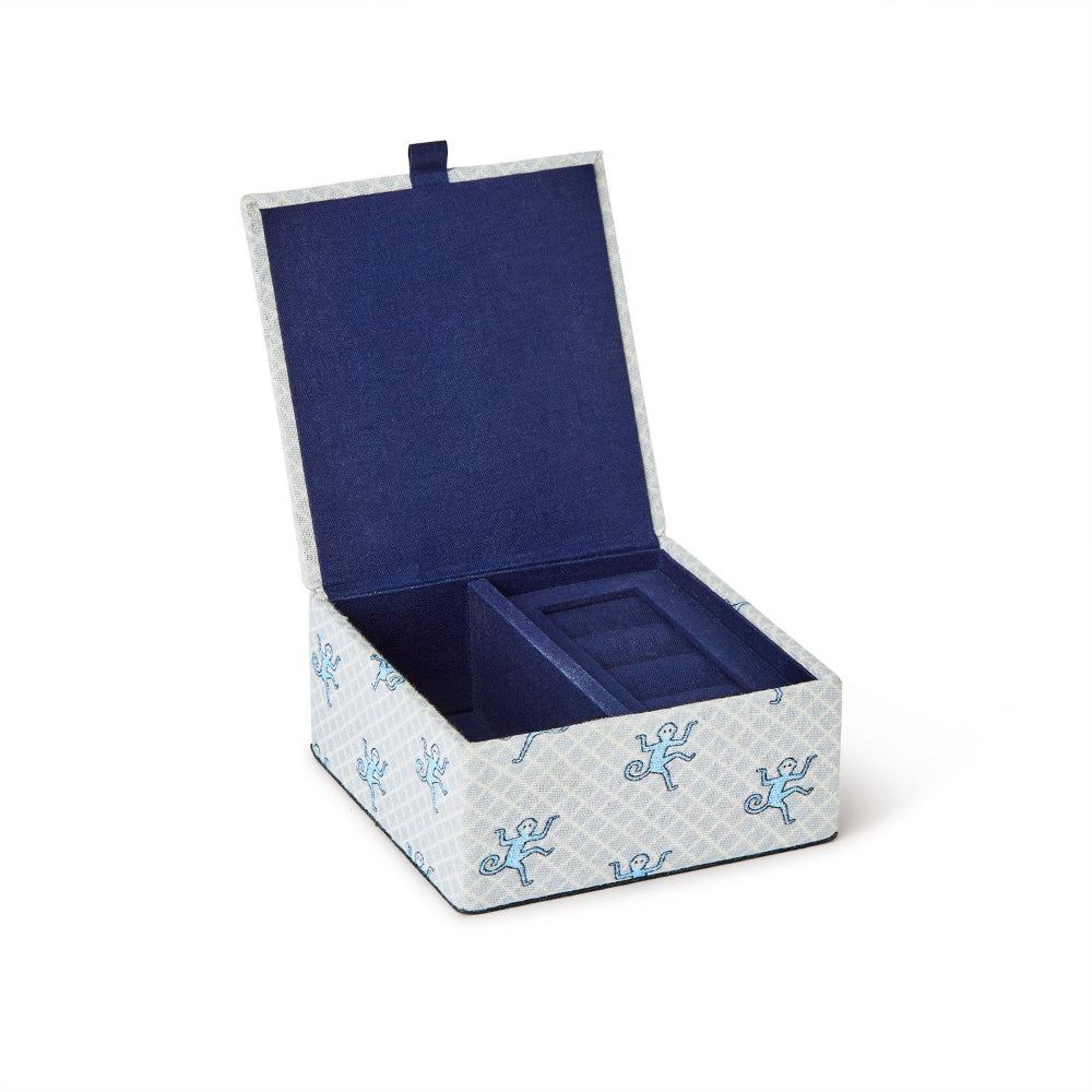 An open jewelry box with a navy blue velvet interior and a light gray patterned exterior decorated with small blue anchors, shown on a white background.