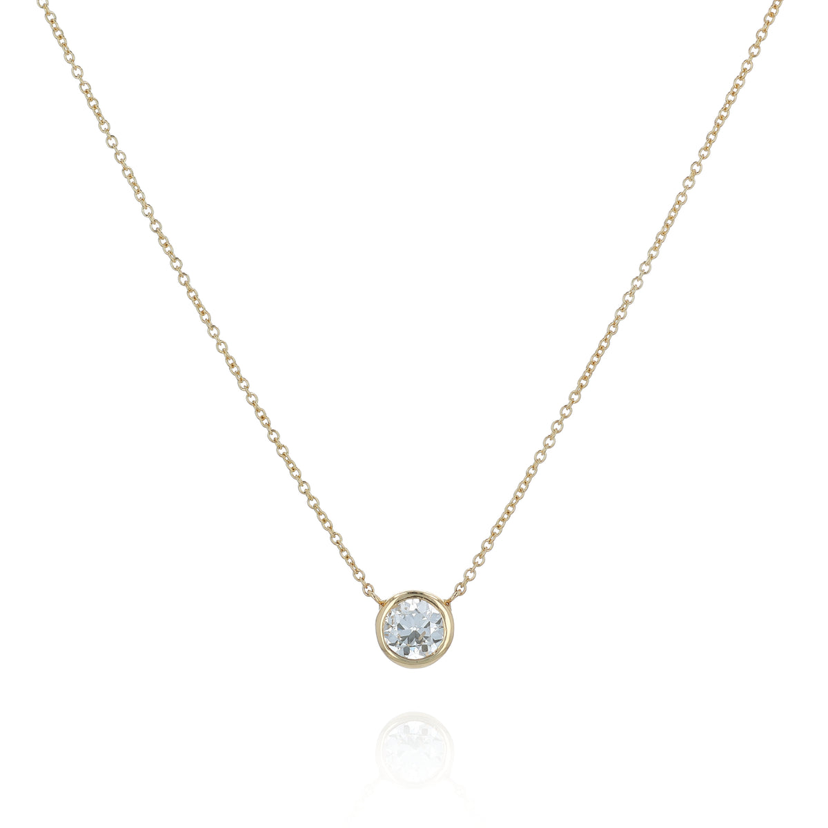 A delicate gold chain necklace with a single bezel-set round diamond pendant, displayed against a clean white background with a soft reflection below.
