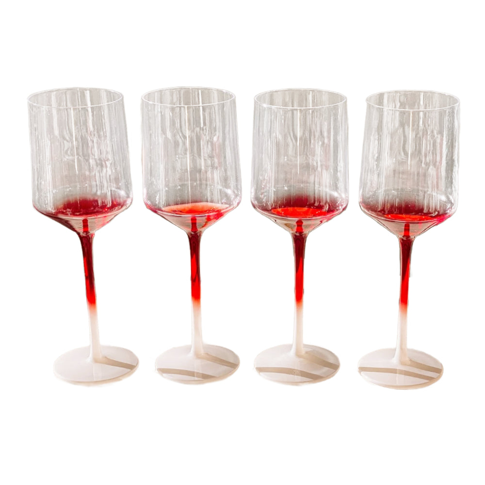 Four clear wine glasses with a deep red tint concentrated at the base of the stems and feet, arranged in a row against a plain white background.