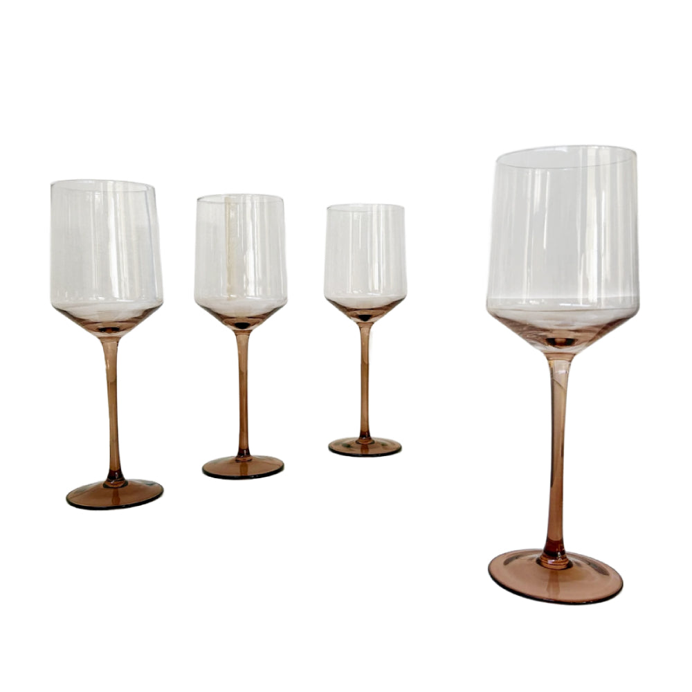 Four clear stemmed wine glasses with a smoky amber-brown tint at the base and stems, arranged on a plain white background.
