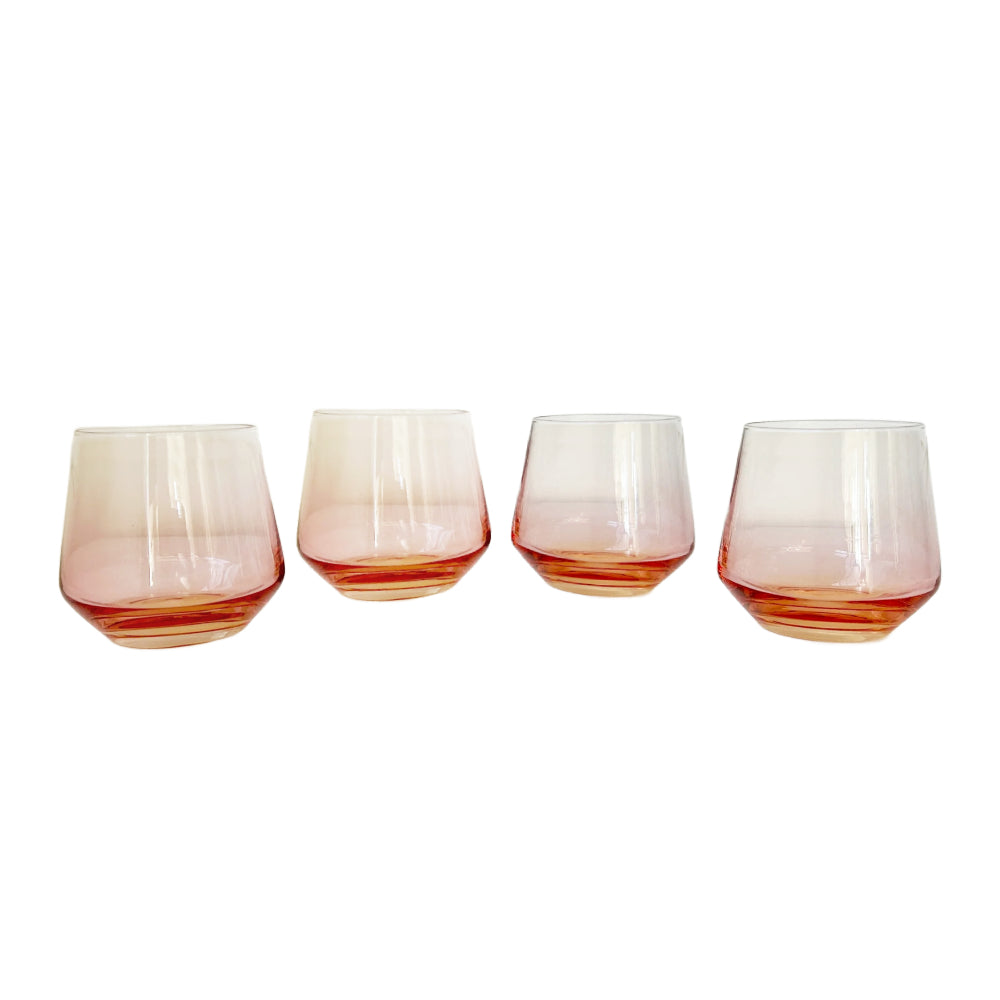 Four stemless tumbler glasses with a gradient design that fades from translucent pink at the top to a warm amber-orange at the bottom, arranged in a row against a solid white background.