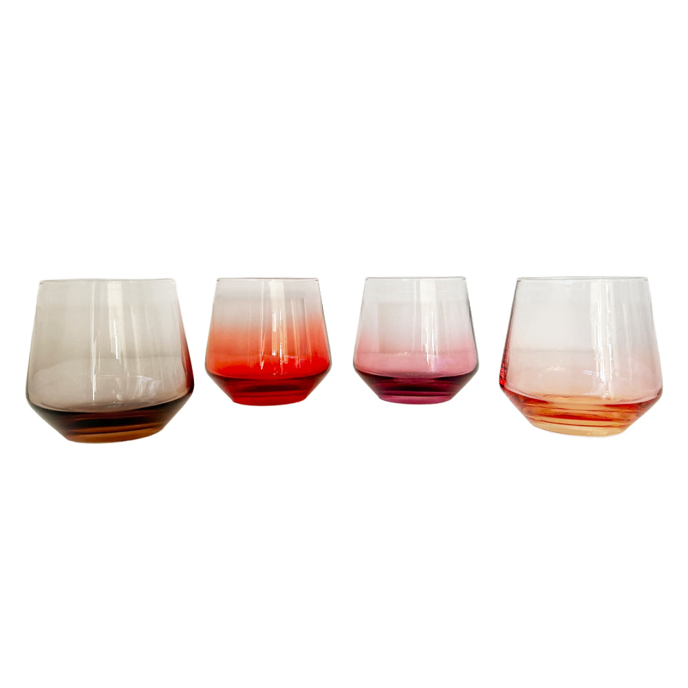 Four stemless glass tumblers with ombre gradients in different colors (brown, red, purple, and orange) arranged in a row against a white background.