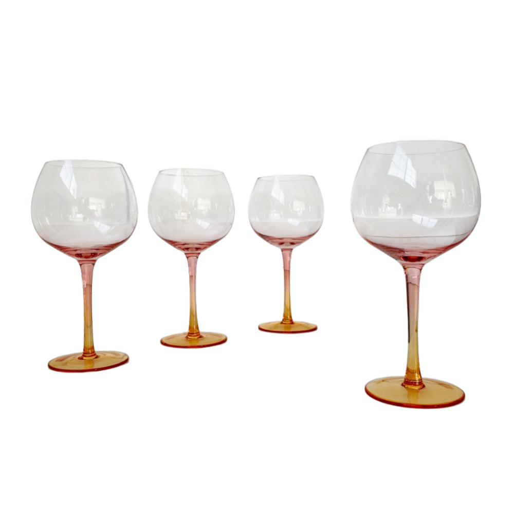 Four clear wine glasses with pink-orange tinted stems and bases, arranged in descending size order against a plain white background.