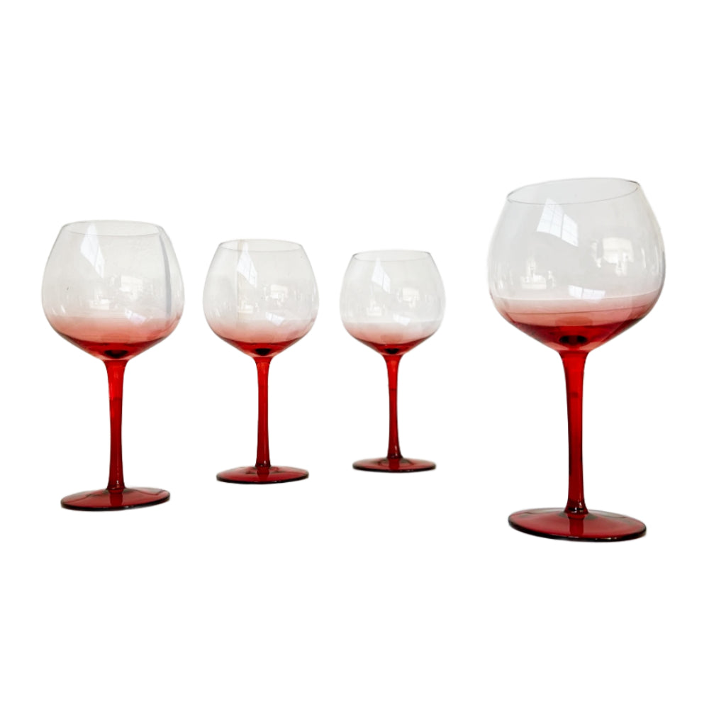 Four stemmed wine glasses with clear bowls fading into a deep red tint at the base and stems, arranged against a plain white background.