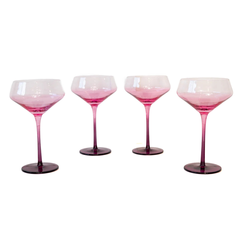 Four pink gradient coupe glasses with dark purple stems and bases, arranged in a row against a plain white background.