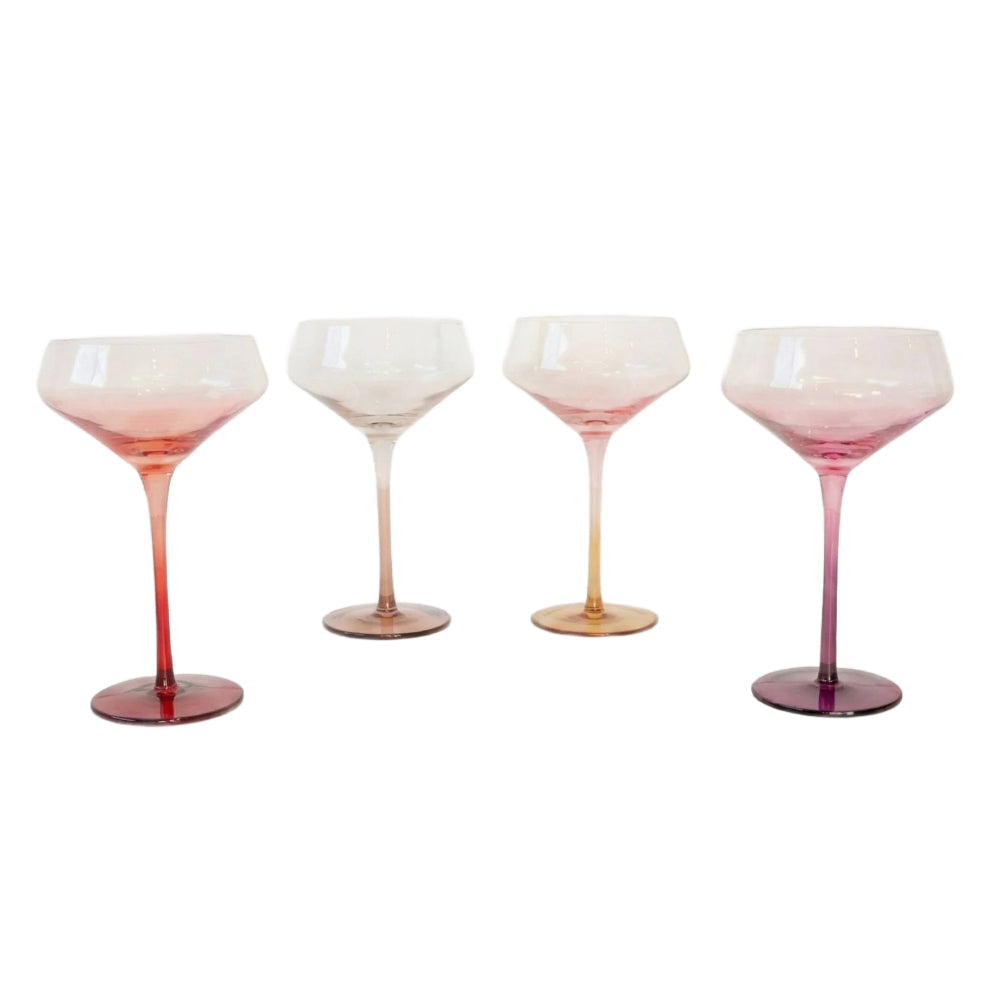 Four stemmed cocktail glasses with gradient pink and orange coloring, arranged in a row against a plain white background.