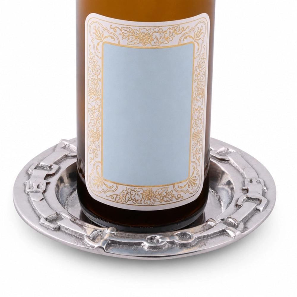 A close-up of a brown glass bottle with a blank light blue label framed by an ornate gold border, resting on a round silver metal base against a white background.
