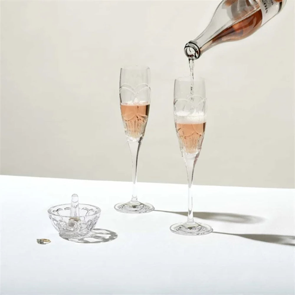 Champagne being poured into two flutes on a white surface with a neutral background