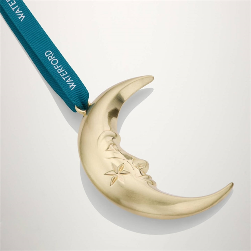 A gold crescent moon ornament with a small star detail, hanging from a teal ribbon printed with the brand name Waterford, set against a clean white background.