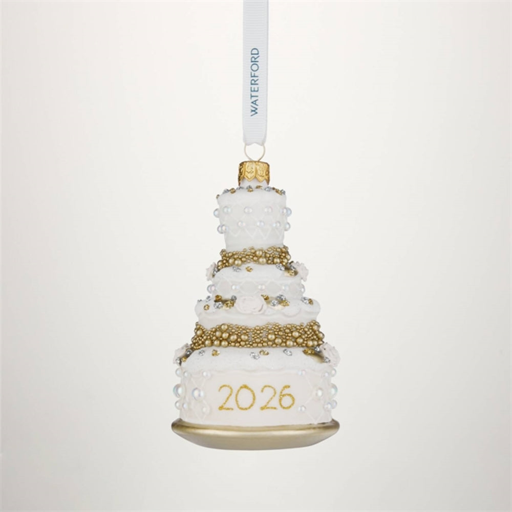 A white and gold tiered cake-shaped hanging ornament with pearl-like bead details, the year '2026' in gold on the base, and a white hanging ribbon printed with the brand name WATERFORD.