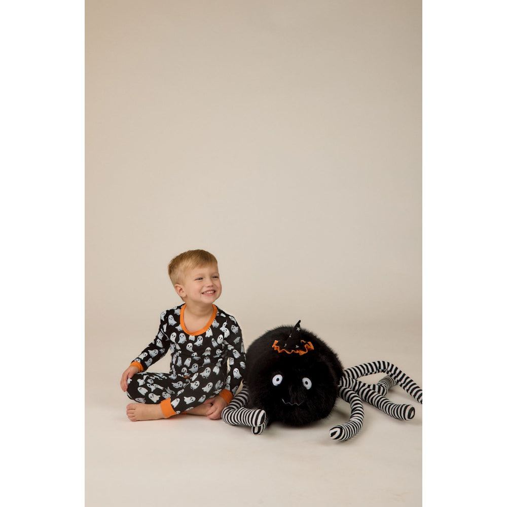 Child in Halloween-themed pajamas sitting next to a large spider plush toy on a beige background