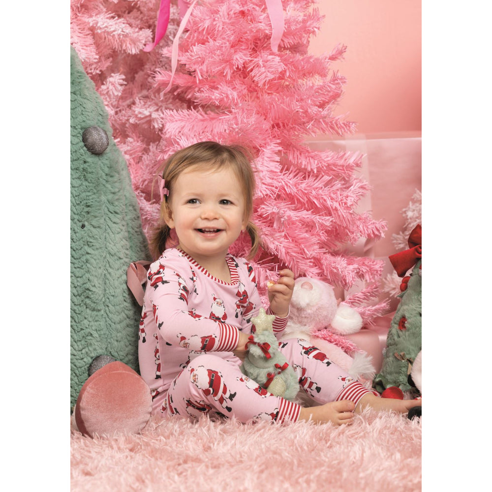 Child in pink pajamas sitting in front of a pink Christmas tree.