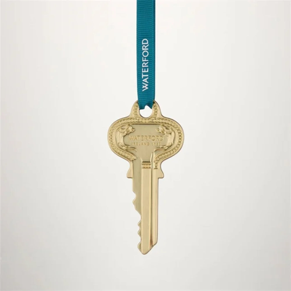 A gold-colored key-shaped ornament or medal hanging from a teal ribbon printed with the brand name 'WATERFORD' in white, set against a clean light gray background.