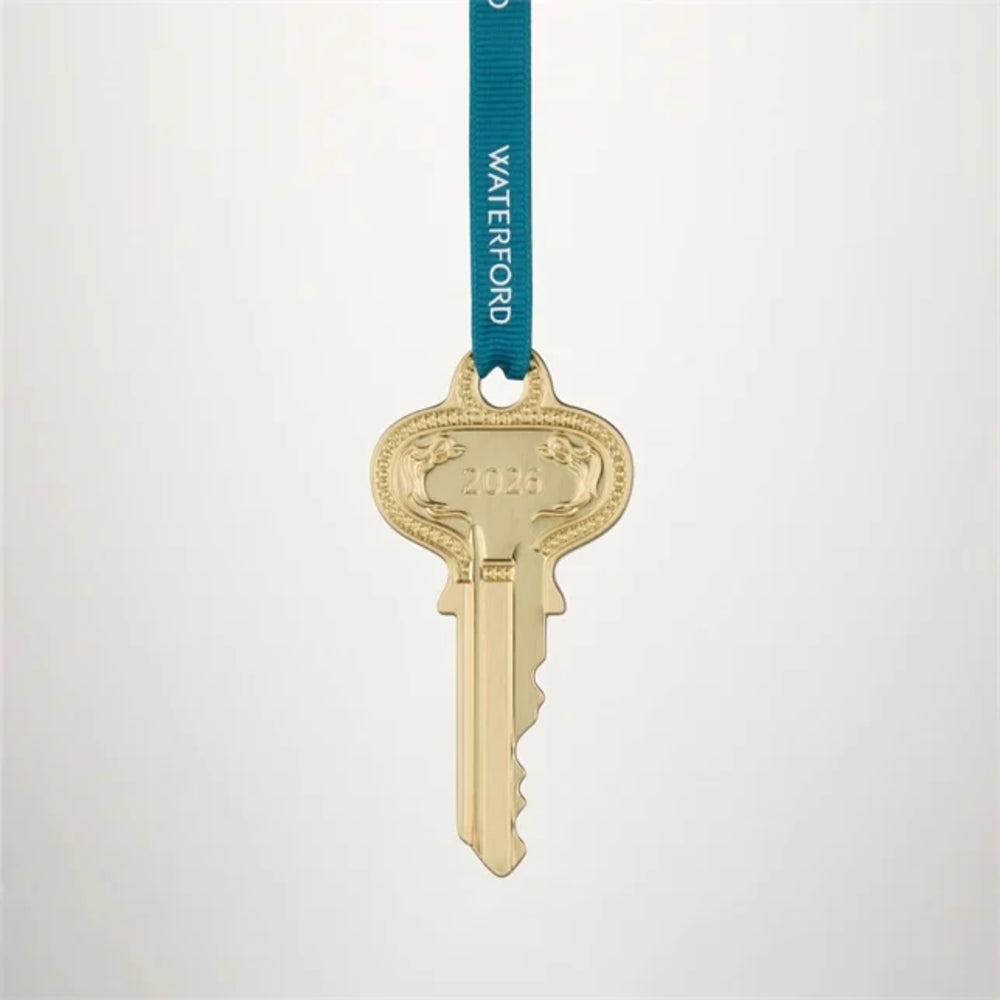 A gold-colored replica key ornament hanging from a teal blue ribbon printed with the name 'WATERFORD' in white capital letters, set against a plain light gray background.