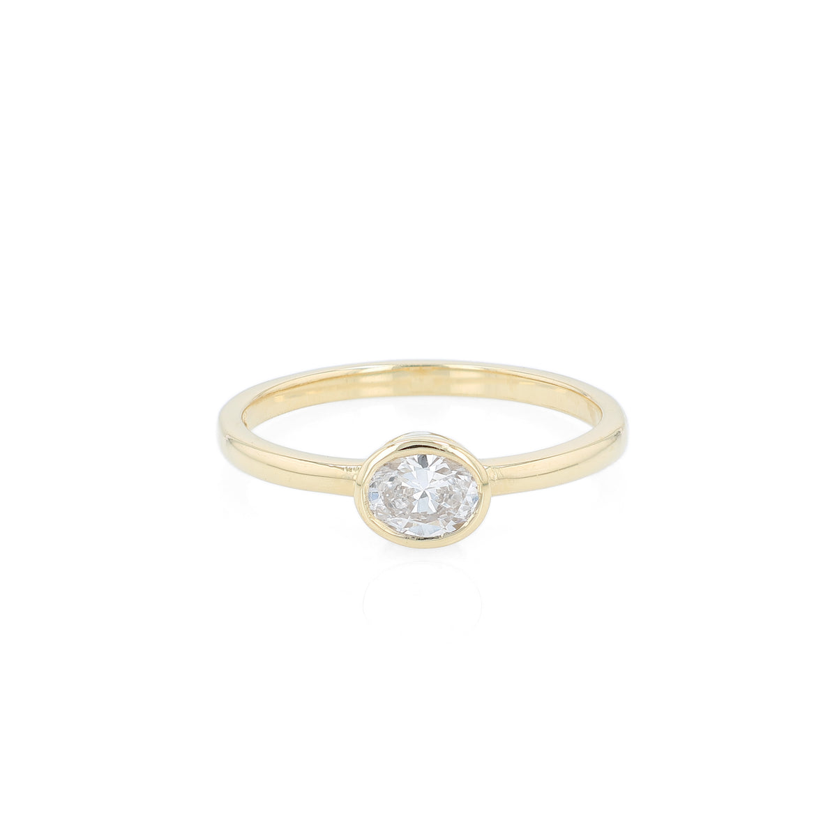 A delicate yellow gold ring featuring a bezel-set oval diamond, shown against a plain white background.