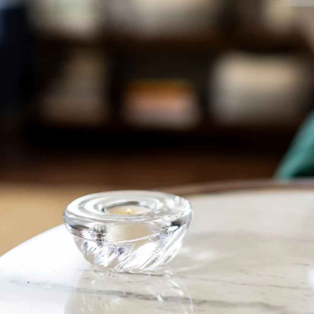 Clear glass candle holder on a reflective surface with a blurred background