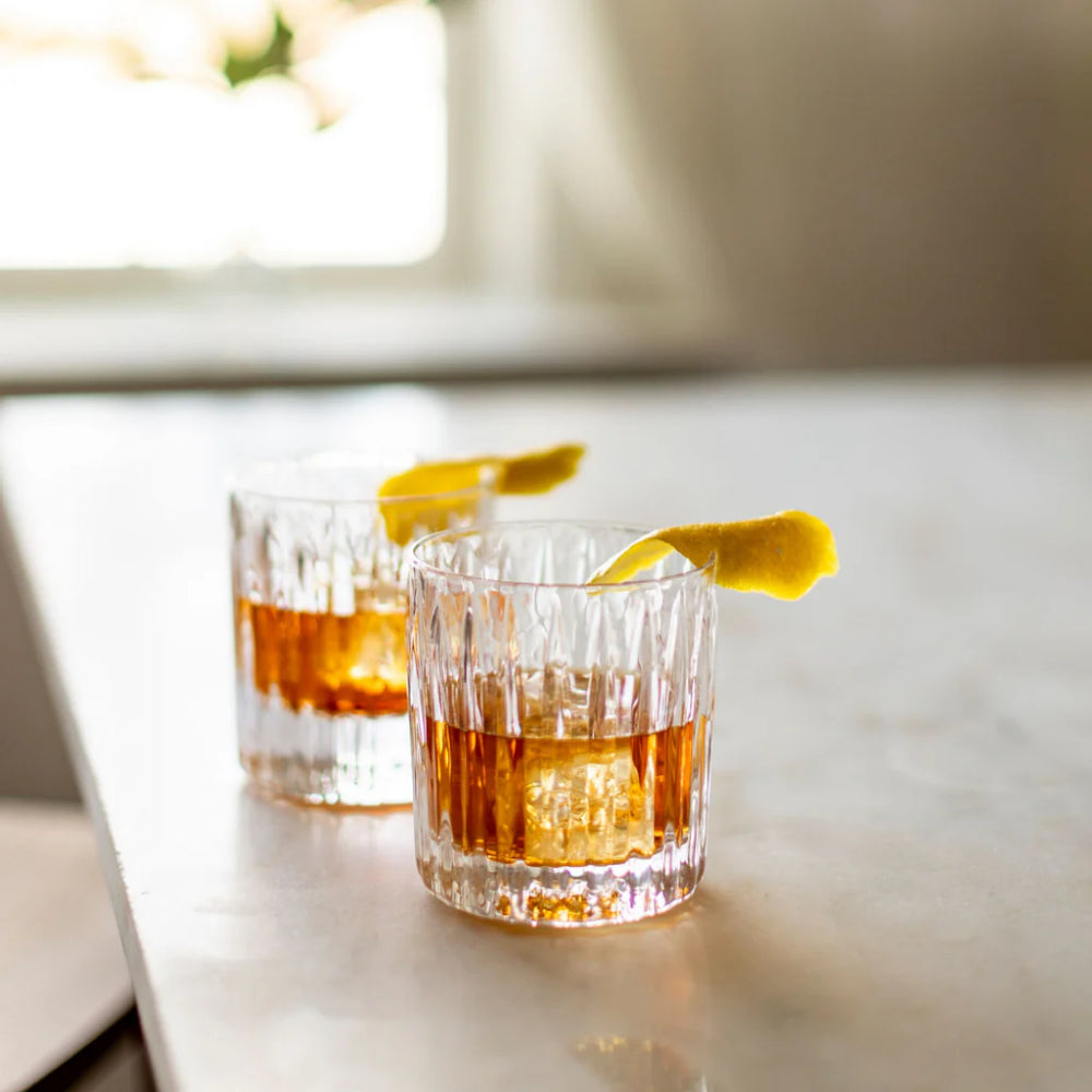 Two glasses of whiskey with lemon wedges on a marble surface.