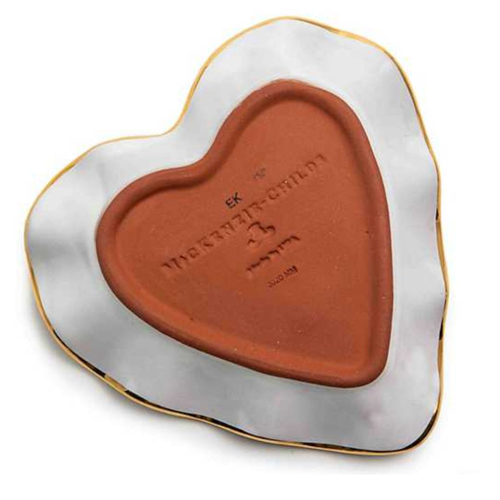 A heart-shaped ceramic plate with a glossy white glaze, a thin gold rim, and a terracotta-colored clay center embossed with Hebrew and English text.