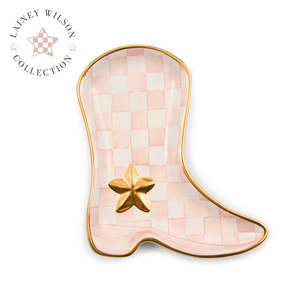 A boot-shaped ceramic dish from the Lainey Wilson Collection, featuring a light pink and white checkerboard pattern, a metallic gold border, and a gold star accent on the front.
