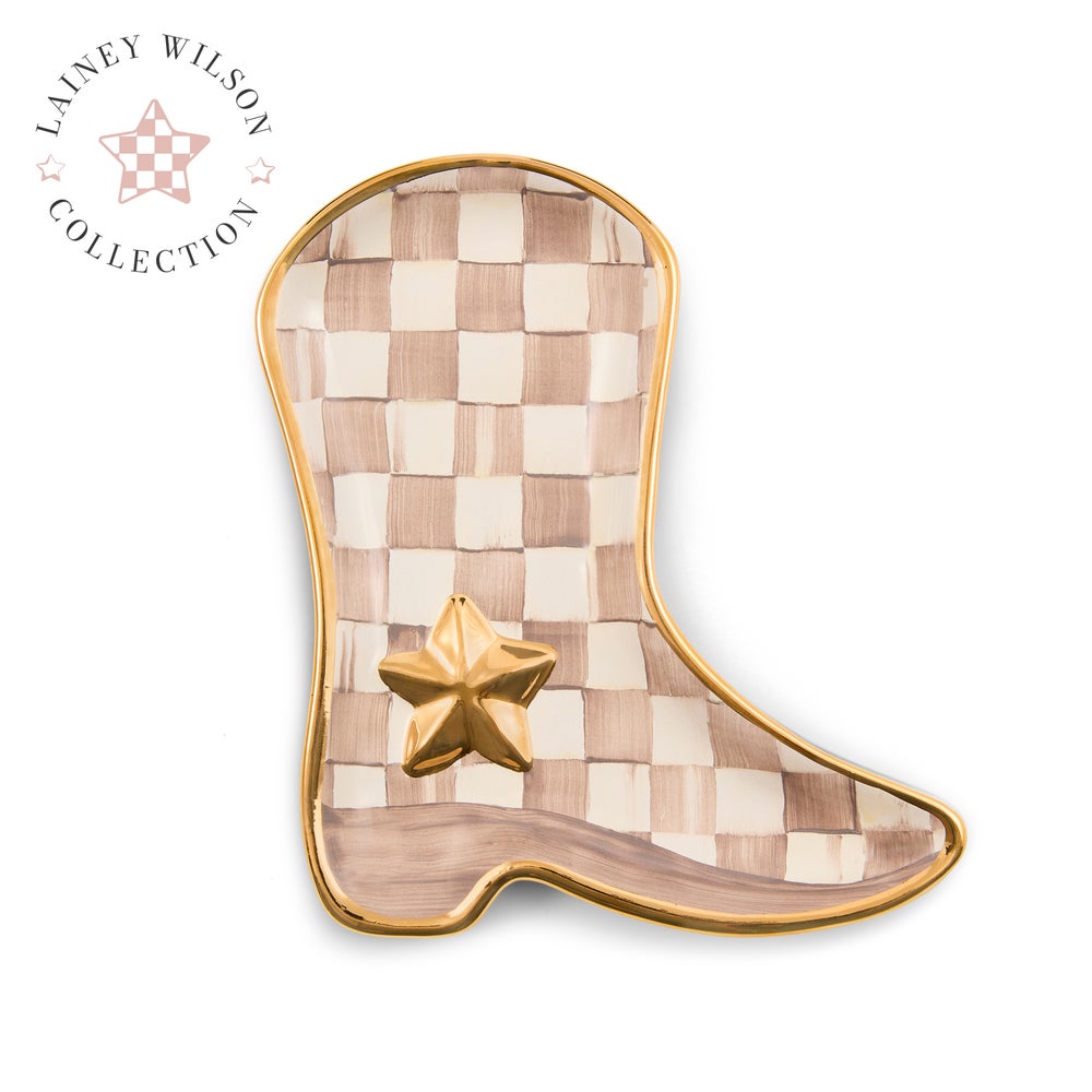 A cowboy boot-shaped decorative tray with a beige and white checkerboard pattern, a metallic gold border, and a gold star accent, shown on a white background with a Lainey Wilson Collection logo in the top left corner.
