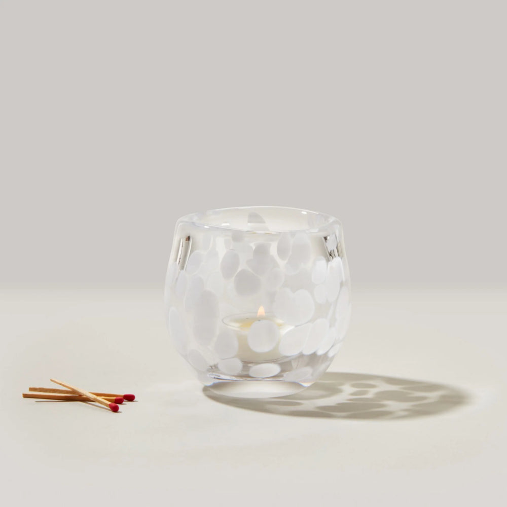 Clear glass candle holder with a small candle inside on a light gray background