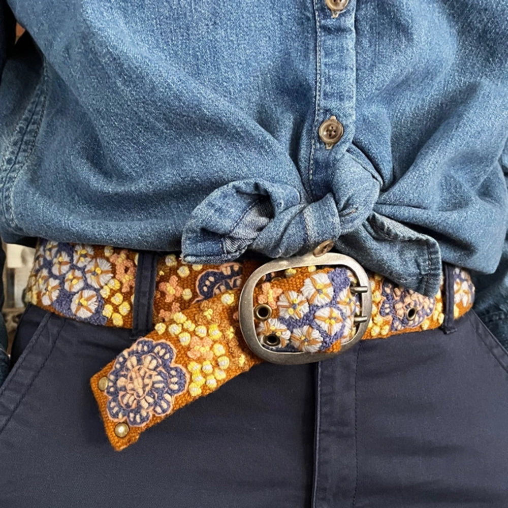 Person wearing a floral-patterned belt with a blue shirt and dark pants.
