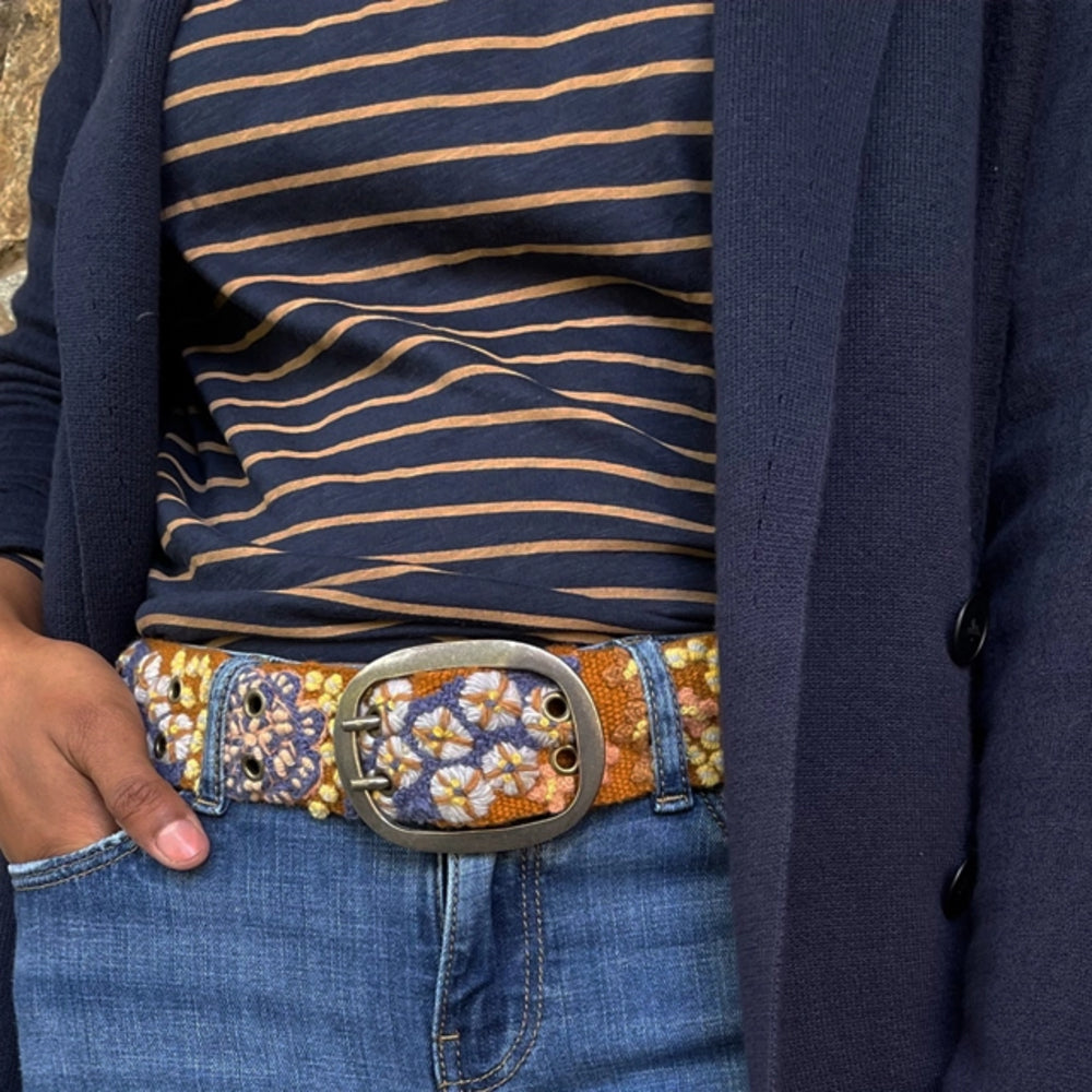 Person wearing a floral-patterned belt with a decorative buckle, striped shirt, and dark jacket.