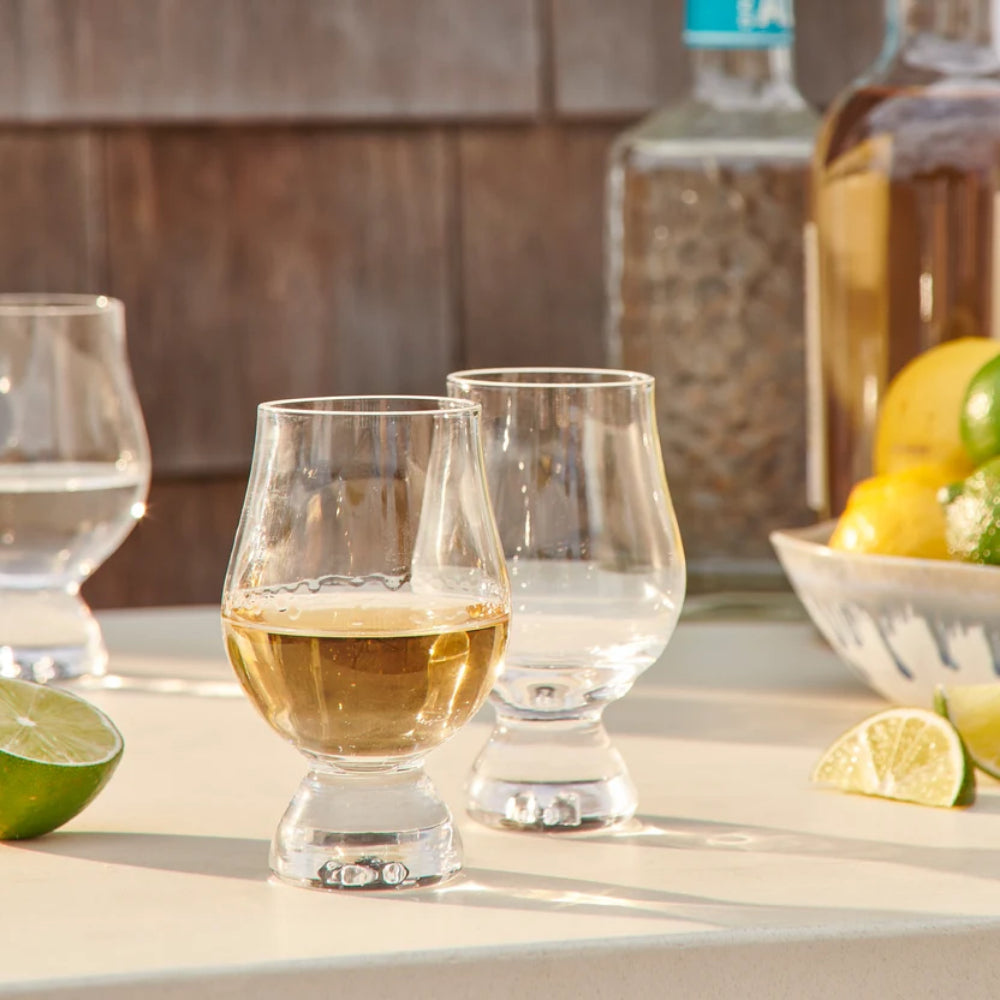 Two clear glass tasting glasses on a with wine in them on a table outside.