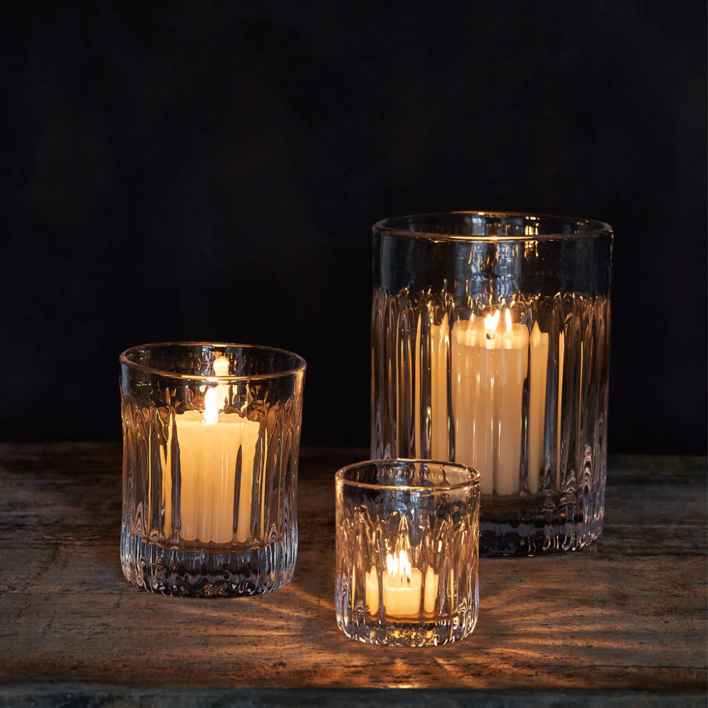 Three glass candle holders with lit candles on a wooden surface against a dark background