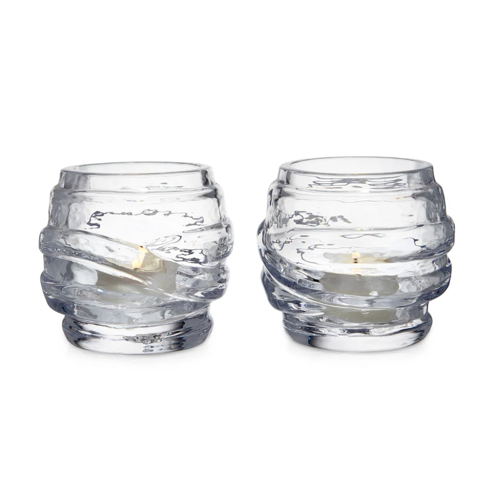 Two ribbed clear glass candle holders with twisted, layered textures, each containing a white taper candle, set against a plain white background.