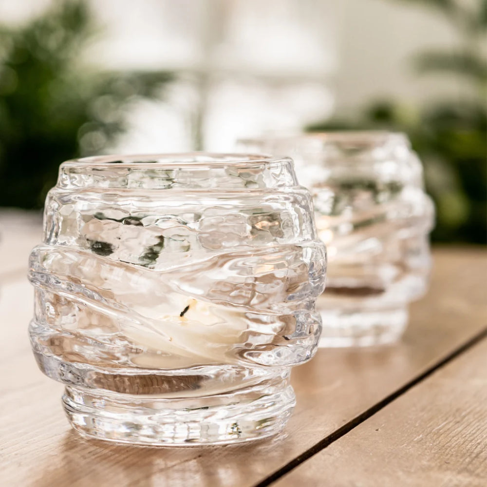 Clear glass candle holders with candles on a wooden surface outdoors.