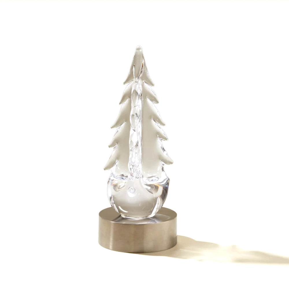 A clear glass Christmas tree with a textured, faceted body, mounted on a brushed brass cylindrical base, set against a plain white background with a soft shadow.