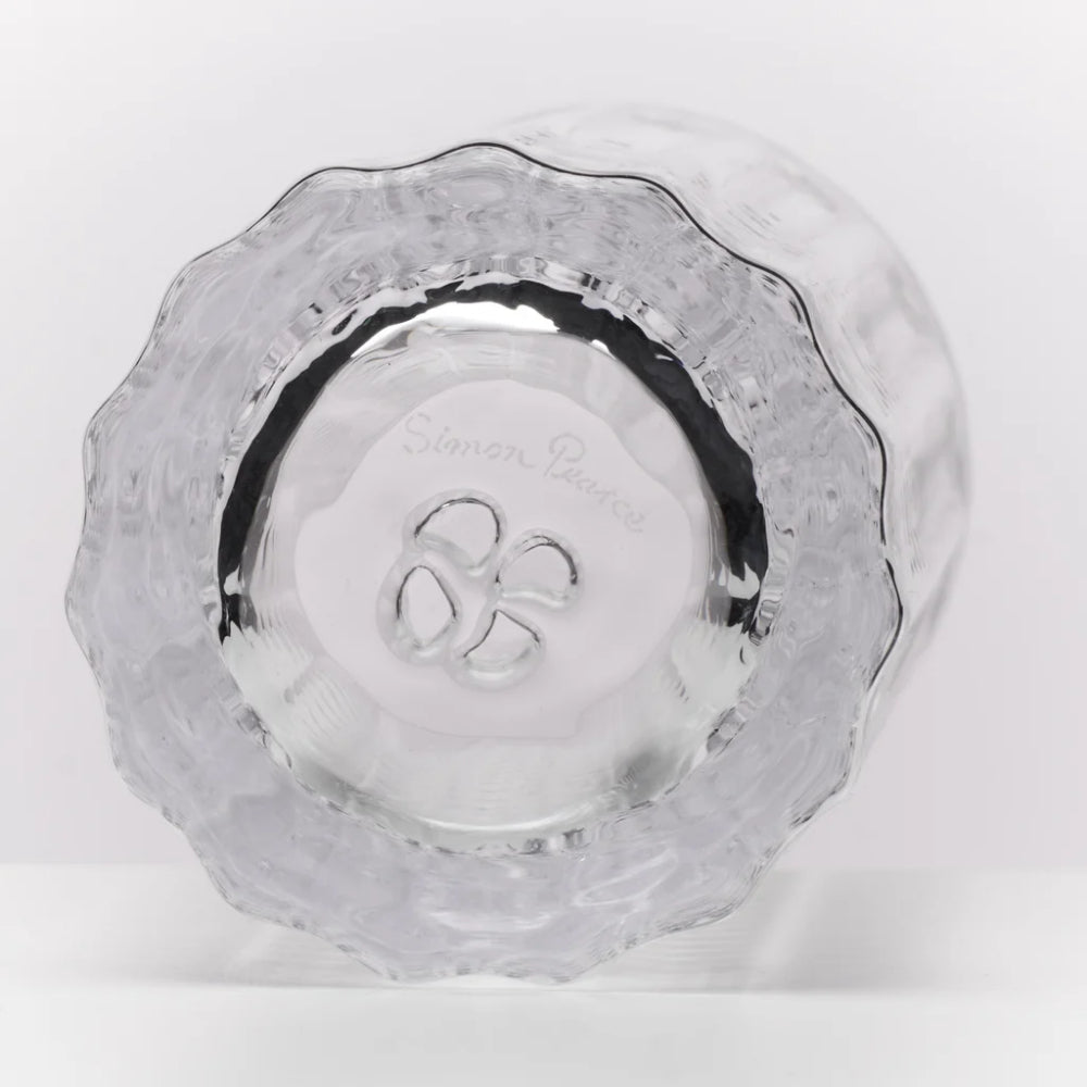 A clear glass tumbler with a textured, scalloped rim and a hammered pattern on the interior, featuring an etched 'Simon Pearce' logo in the center, shown on a white background.