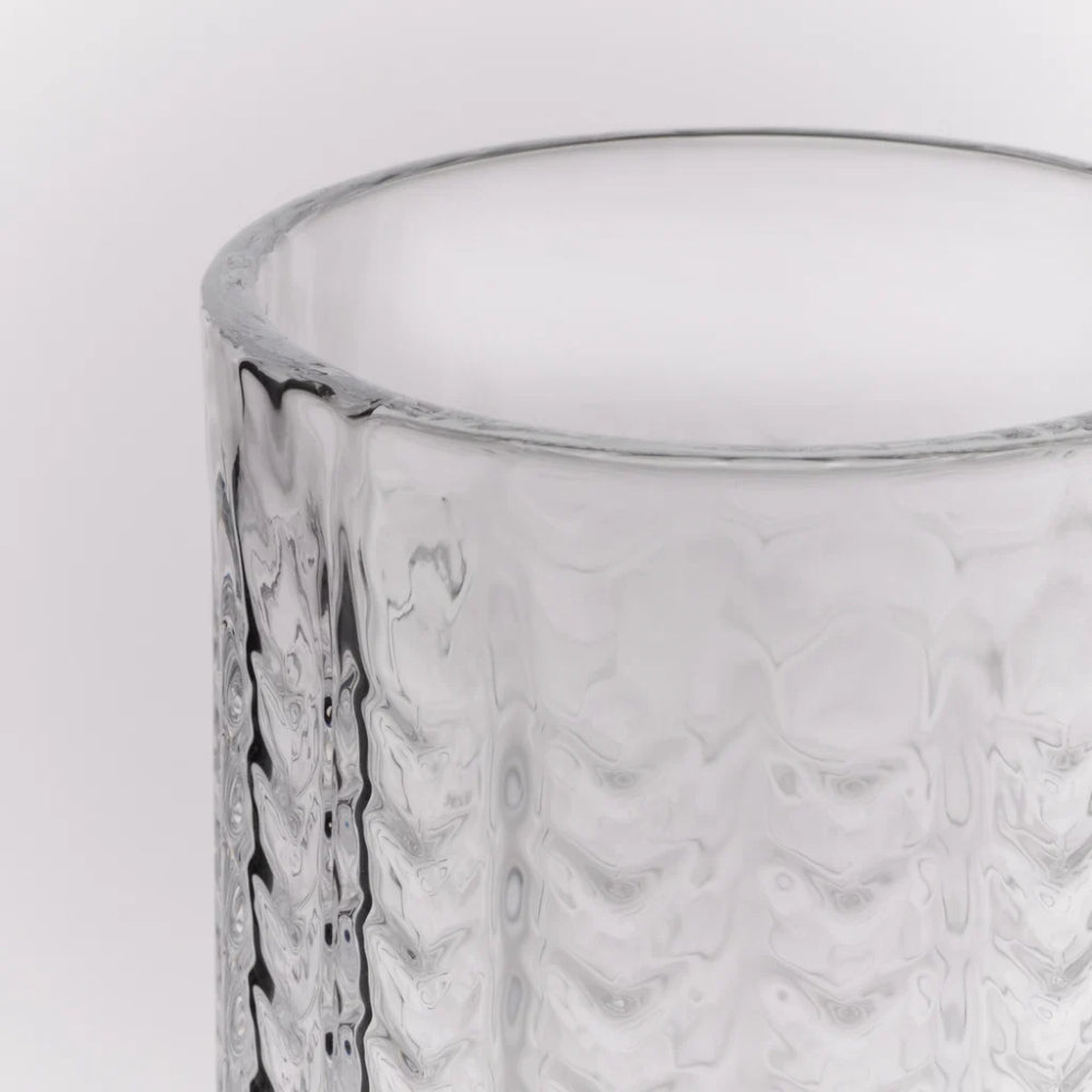Close-up of a clear textured glass tumbler with a wavy embossed pattern, showing the rim against a light gray background.