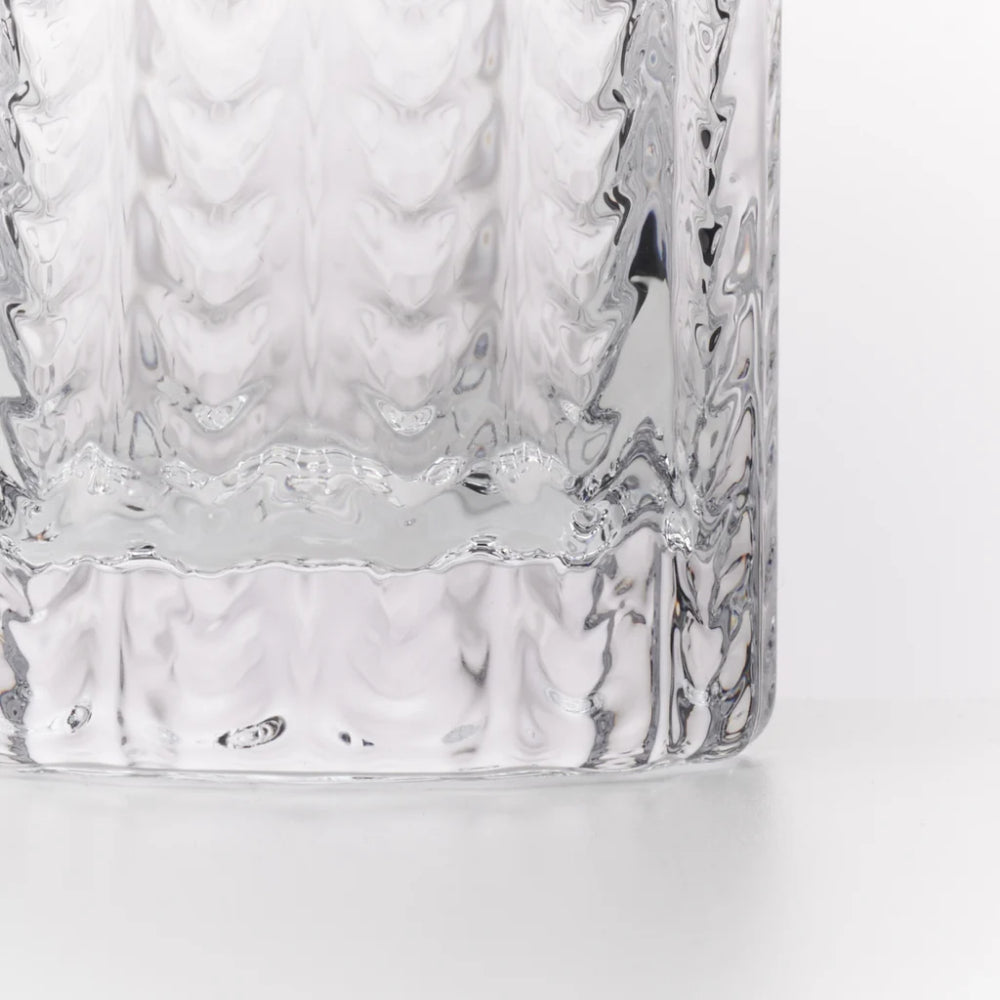 A close-up of a clear textured glass tumbler showing the wavy, embossed pattern on the side and a flared, ribbed base against a white background.