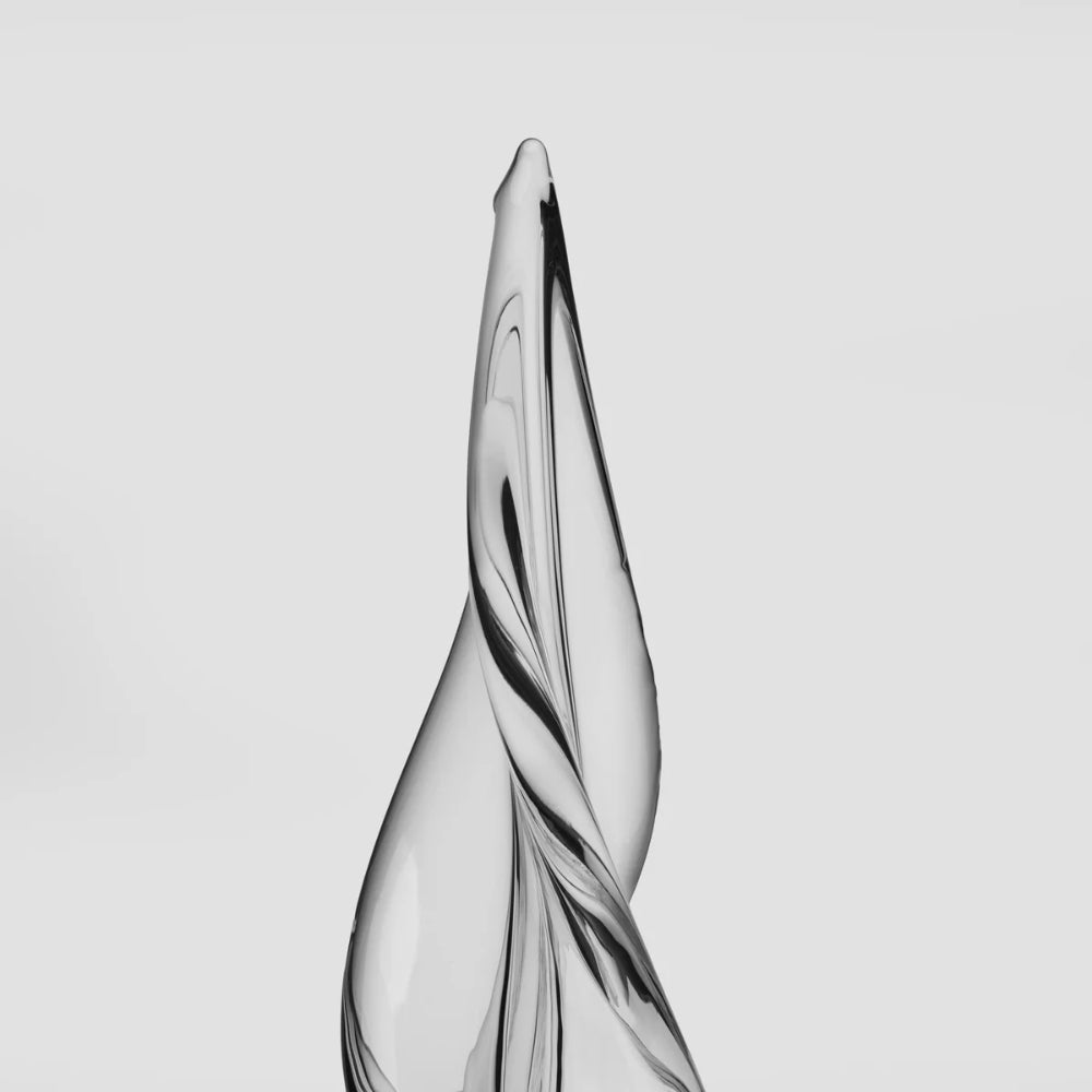 A modern, glass sculpture with a twisted, teardrop-like form and glossy black swirls, shown against a solid light gray background.