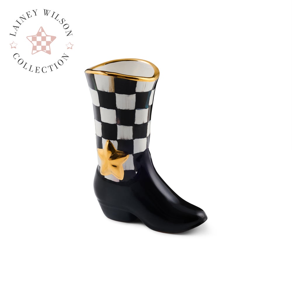 A ceramic cowboy boot planter from the MacKenzie Childs Lainey Wilson Collection, featuring a black and white checkerboard pattern on the shaft, a black polished finish on the foot, and gold accents including a star and rim.