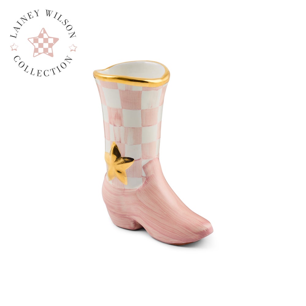 A ceramic cowboy boot planter from the MacKenzie Childs Lainey Wilson Collection, featuring a pink and white checkerboard pattern on the shaft, a pink brushed finish on the foot, and gold accents including a star and rim.